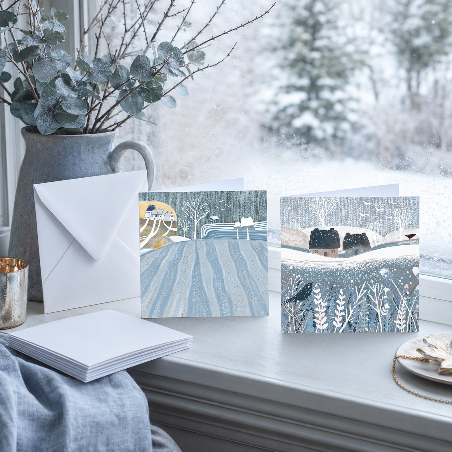 Winter Fields pack of four Christmas cards with snowy landscape designs and white envelopes on a winter windowsill