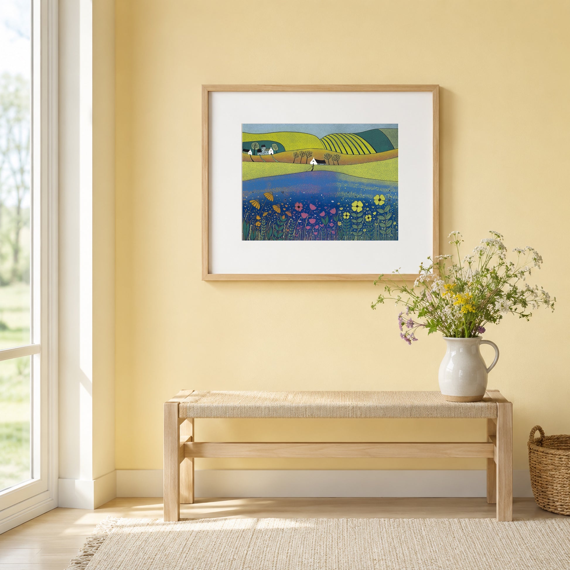 Sea of Tranquility print framed in oak on a warm yellow wall above a wooden bench with a jug of wildflowers.