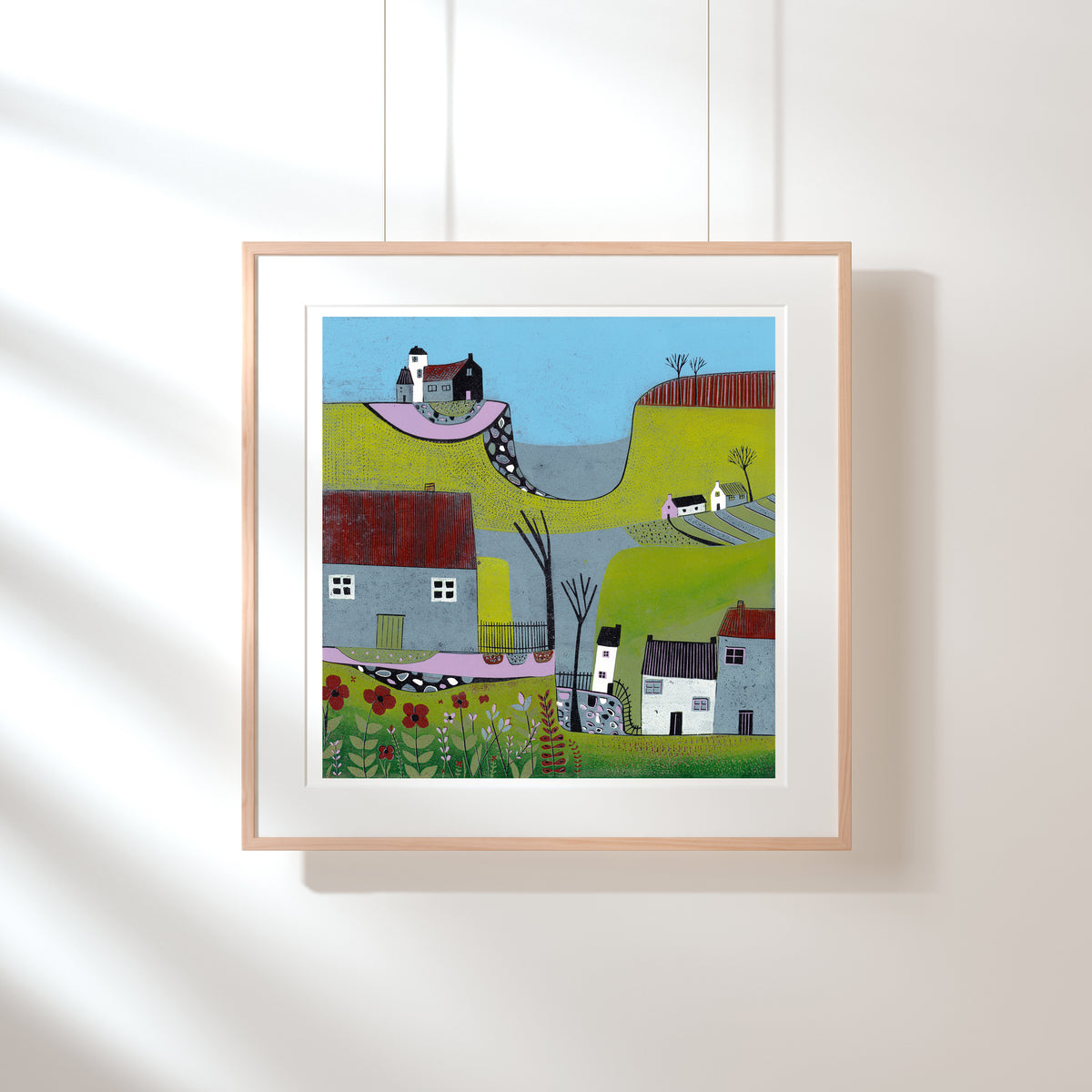 The Hills Above the Shore square linocut print shown framed with a wide white mount